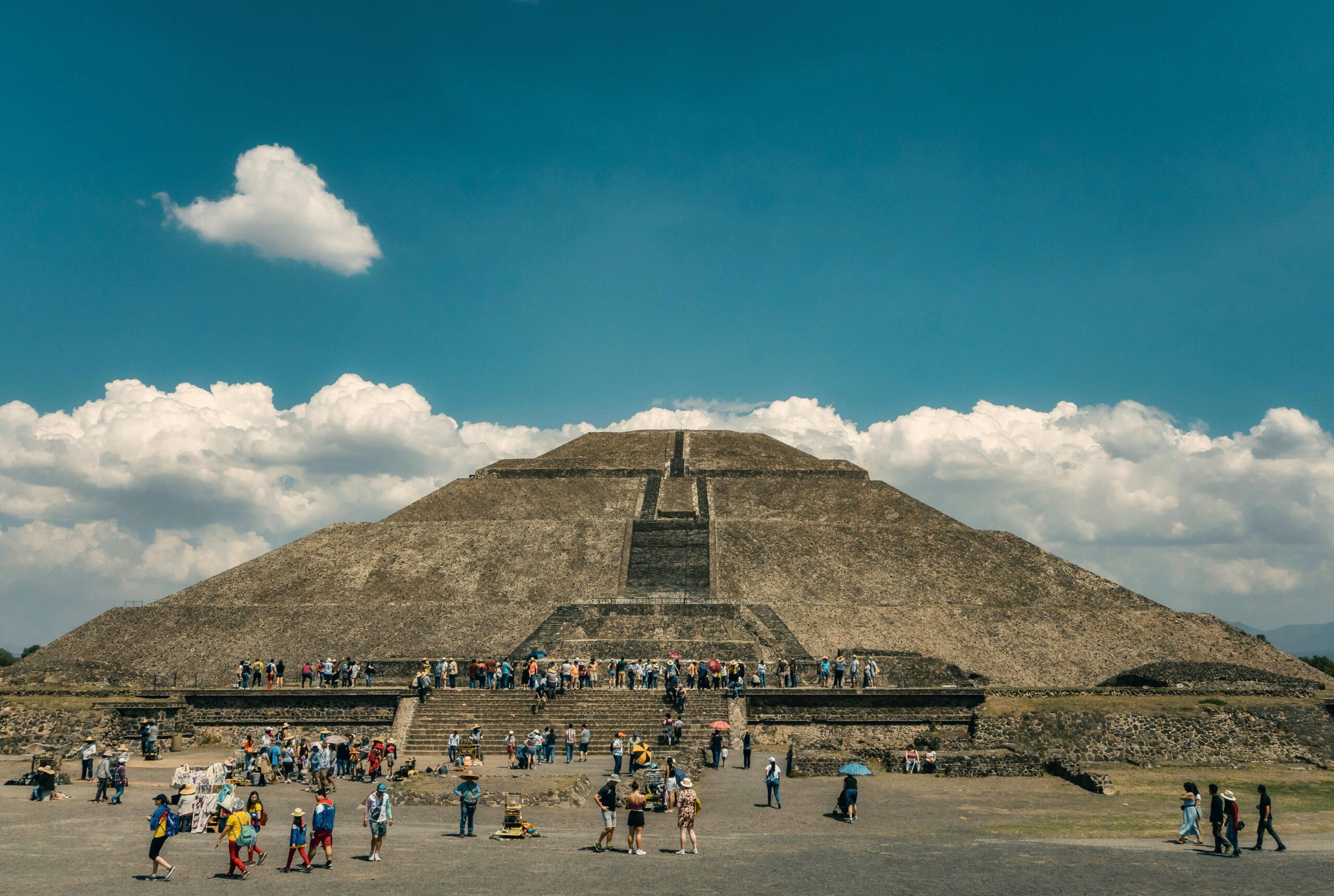 Crowds gather at the iconic Pyramid of the Sun in Teotihuacan under a clear blue sky.